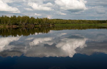 Forest lake view, smooth surface of a lake with clouds reflected, shining level of a forest lake
