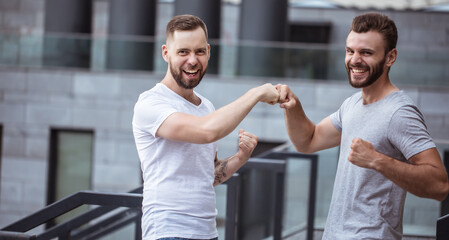 Two happy excited modern bearded best friends in casual clothes having fun and chatting together outdoors.