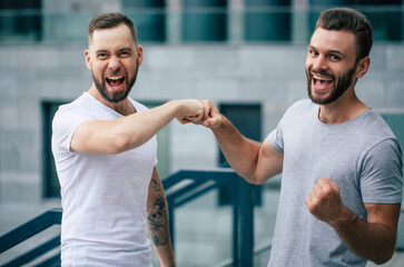 Two happy excited modern bearded best friends in casual clothes having fun and chatting together...