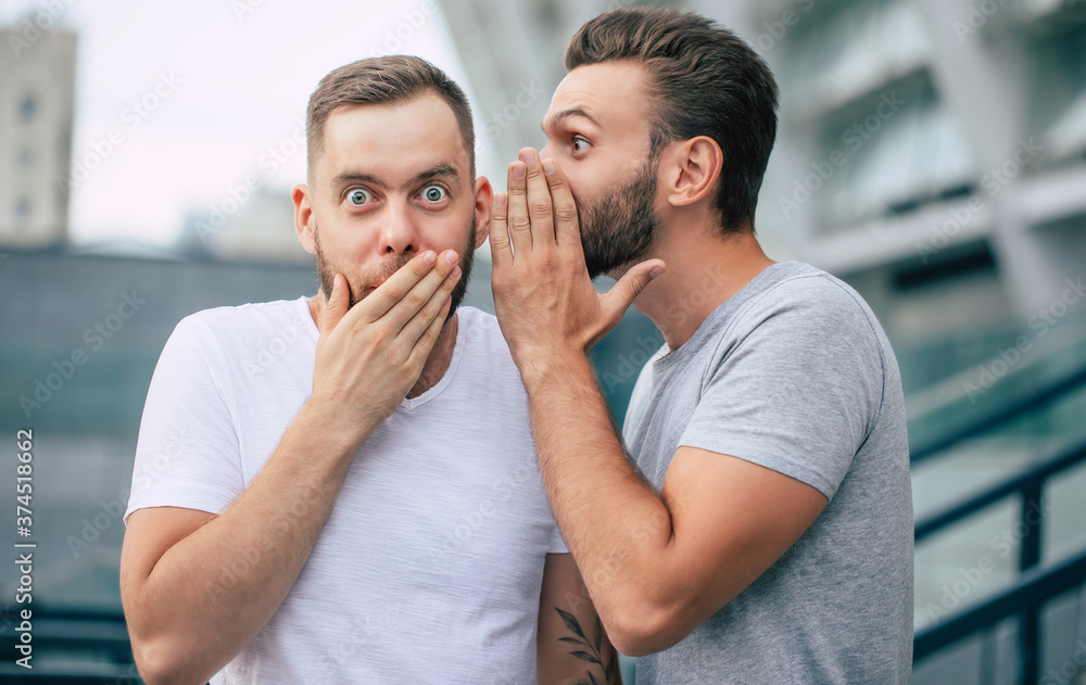 Wall mural two funny excited best friends in casual clothes are gossiping and chatting together outdoors.