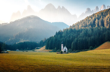 Fototapeta na wymiar Incredible landscape with cloudy sky over the Dolomites mountains. Fantastic summer View on mountain valley with green grass under sunlight and famouse church in Santa Maddalena village in sunny day