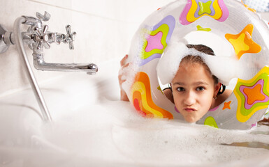 Funny little girl bathes in a bathtub with an inflatable lifebuoy