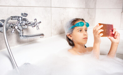 Focused little caucasian girl in swimming goggles does a selfie