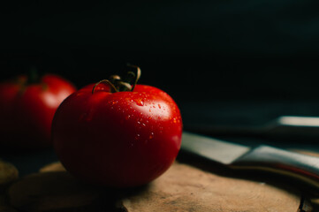 Red tomatoes on a black background, two steel knives are lying nearby. High quality photo