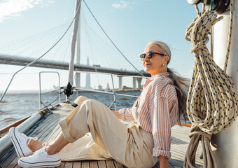 Stylish mature woman sitting on a yacht bow. Senior female enjoying vacation on a private sailboat.