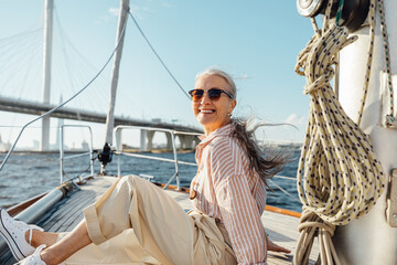 Happy mature woman wearing sunglasses on a sailboat and looking at camera. Senior female sitting on...