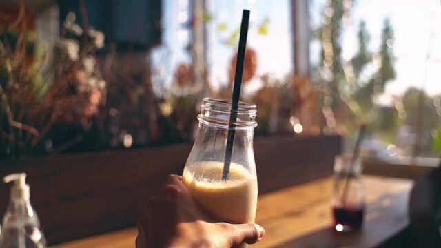 A girl shows off a beautiful glass of cold frappe coffee on a bright sunny summer day Hand close up Slow motion