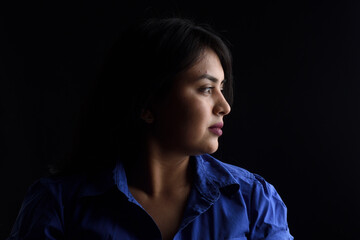side view of dark portrait of a latin woman on black background, serious