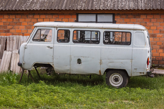 An old Soviet minibus without wheels is parked in the village yard