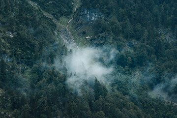 Mist and fog clouds hanging in the mountain on a rainy weather day with mountain and tree shilhouettes. Dramatic mountain view. Austrian Alps, Salzkammergut in Austria, Europe