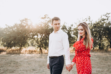 Beautiful couple, a girl in a red dress and a guy in a white shirt, are walking in the park in nature