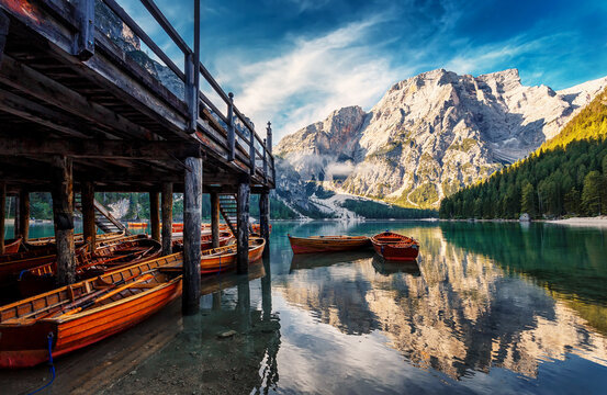 Amazing alpine lake with colorful sky over the majestic mountain during sunrise. Most popular view on Braies lake with wooden boats on calm water. iconic locations for photographers and travelers