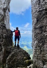 Fototapeta premium Man standing in stone window, mountain view, blue sky, Bavaria, Germany