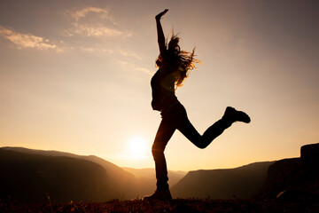 Silhouette einer Frau beim Sprung auf einem Berggipfel © by-studio