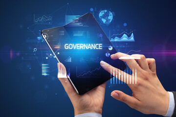 Businessman holding a foldable smartphone with GOVERNANCE inscription, successful business concept