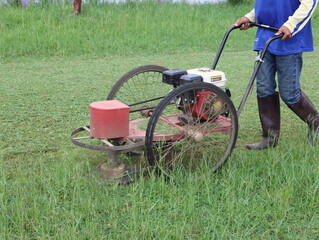 A worker cutting grass wearing blue clothes Wear brown boots cutting grass in garden on daytime