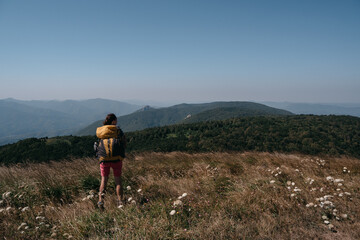 Fototapeta na wymiar Beautiful landscapes of the national Park and human looking at the mountains, forests and hills. A female traveler stands in the mountains with a large yellow Hiking backpack.