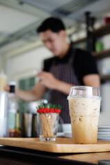 Closed up a plastic glass of latte iced coffee on wooden tray for prepare serving to customers at counter bar in the morning at modern cafe.