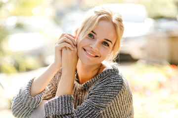 Nice girl in trendy oversized sweater leaned and looking at camera against background of cars with...
