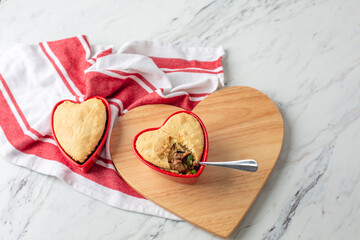 Beef Pot Pies in Red Heart-Shaped Dishes; One with Spoon; On Heart-Shaped Board on White Counter Top