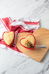 Beef Pot Pies in Red Heart-Shaped Dishes; One with Spoon; On Heart-Shaped Board on White Counter Top