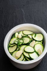 Marinated zucchini slices in clay bowl on black stone background
