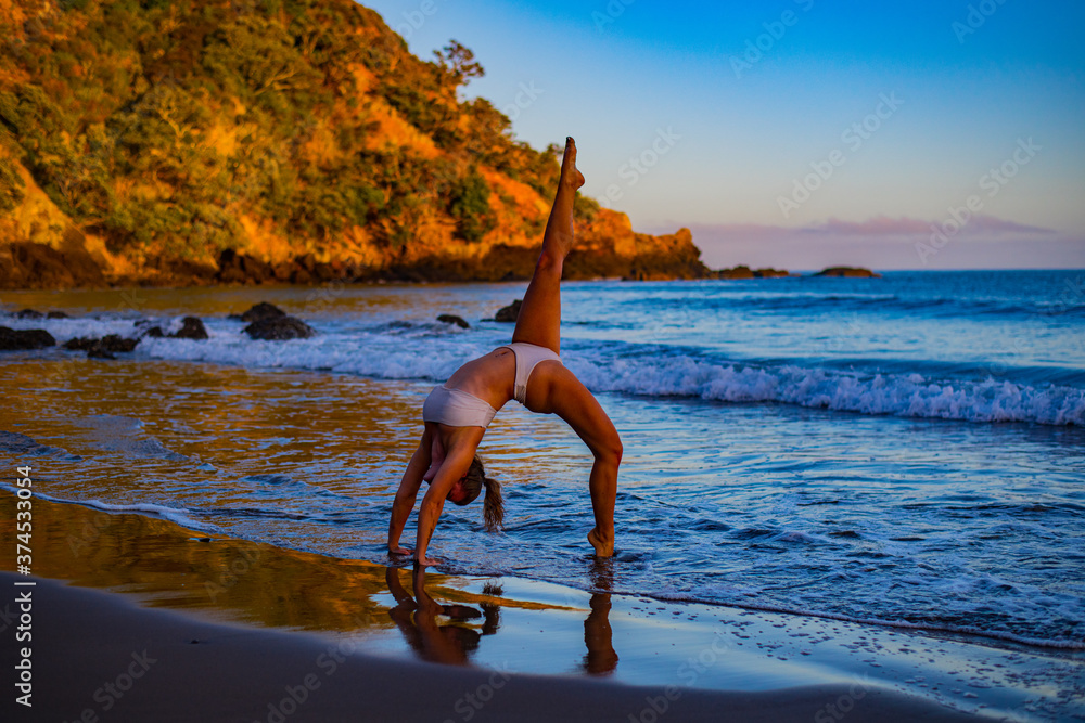 Wall mural young woman doing yoga on the beach