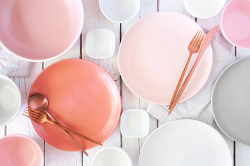 Tableware set in pastel pink, coral, white and grey colors. Above view on a white wood background.