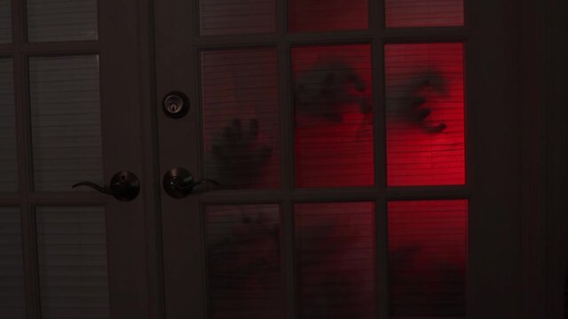 Creepy hands clawing at a bedroom door with red light shining behind it at night