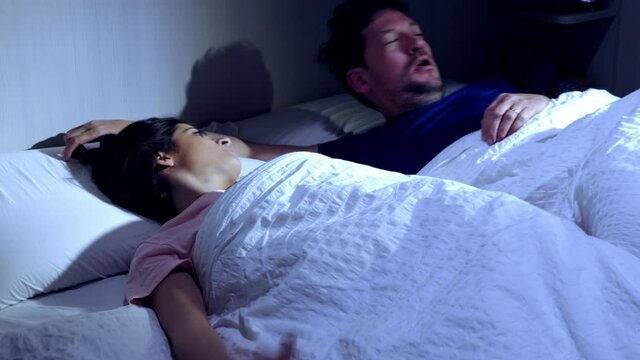 Woman in bed at night waking up two times snoring husband that doesn't let her sleep