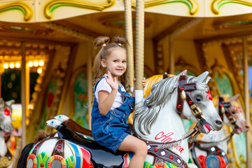 happy baby girl rides a carousel on a horse in an amusement Park in summer