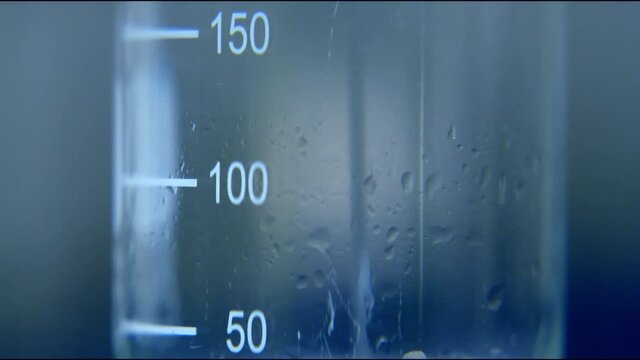 Professional scientific beaker tub glass with metric scale filling with transparent liquid of water viscosity. full frame macro vaccine research concept close up shot with selective focus. 