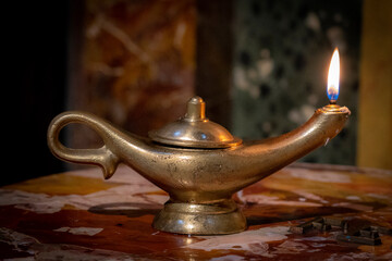 An ancient brass oil lamp burns on a marble table top in a church in Rome, Italy.