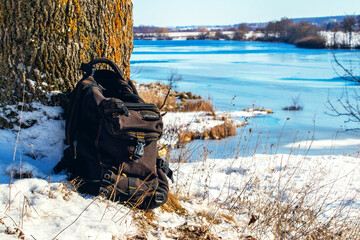 Backpack near a tree on the shore river in winter