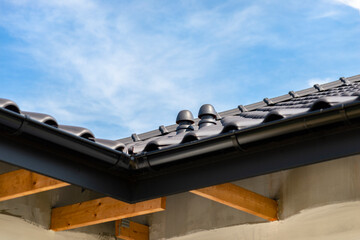 The roof of a single-family house covered with a new ceramic tile in anthracite against the blue sky, visible ceramic ventilation fireplace on the roof.
