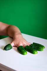 photo hand with cucumbers on fingers green background white table