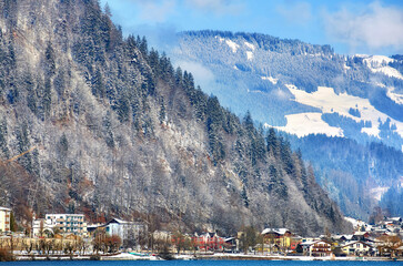 Alps with village houses, snow, forest, blue lake and misty clouds