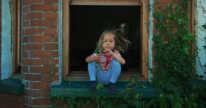 Little preschooler sitting on window sill looking at garden
