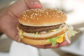 hamburger with beef Patty and salad in a man's hand. Concept of harmful nutrition