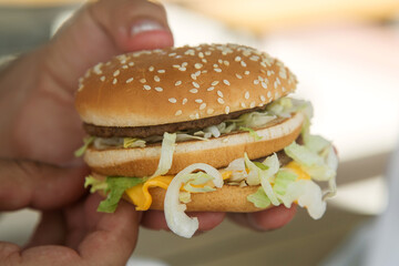 hamburger with beef Patty and salad in a man's hand. Concept of harmful nutrition