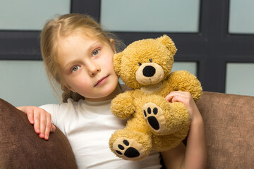 Little girl on sofa hugging teddy bear.