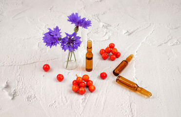 Medical ampules, blue flowers and red berry on white textured background, colorful composition