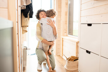 Young mother embracing her cute little son after coming back home from work