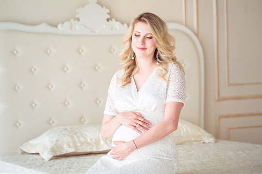 Attractive pregnant woman is sitting in bed and holding her belly. Last months of pregnancy