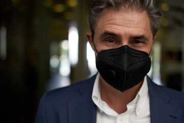 Portrait of man wearing black face mask, looking at camera. Dark, warm colors.