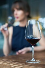 Winetasting concept. Selective focus on wineglass, woman drinking wine in the background.