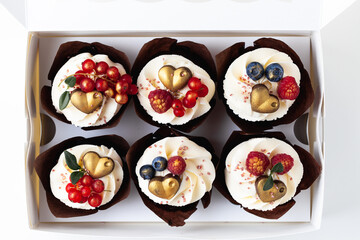 a set of cupcakes decorated with raspberries, redcurrant and blueberries in the white gift box on the white background