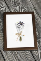 A bouquet of lavender in a photo frame. On brushed pine boards painted black and white.