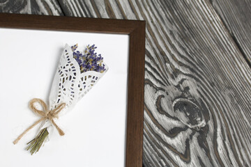 A bouquet of lavender in a photo frame. On brushed pine boards painted black and white.