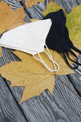 Medical masks in black and white. Among the dried maple leaves. On brushed pine boards painted black and white.